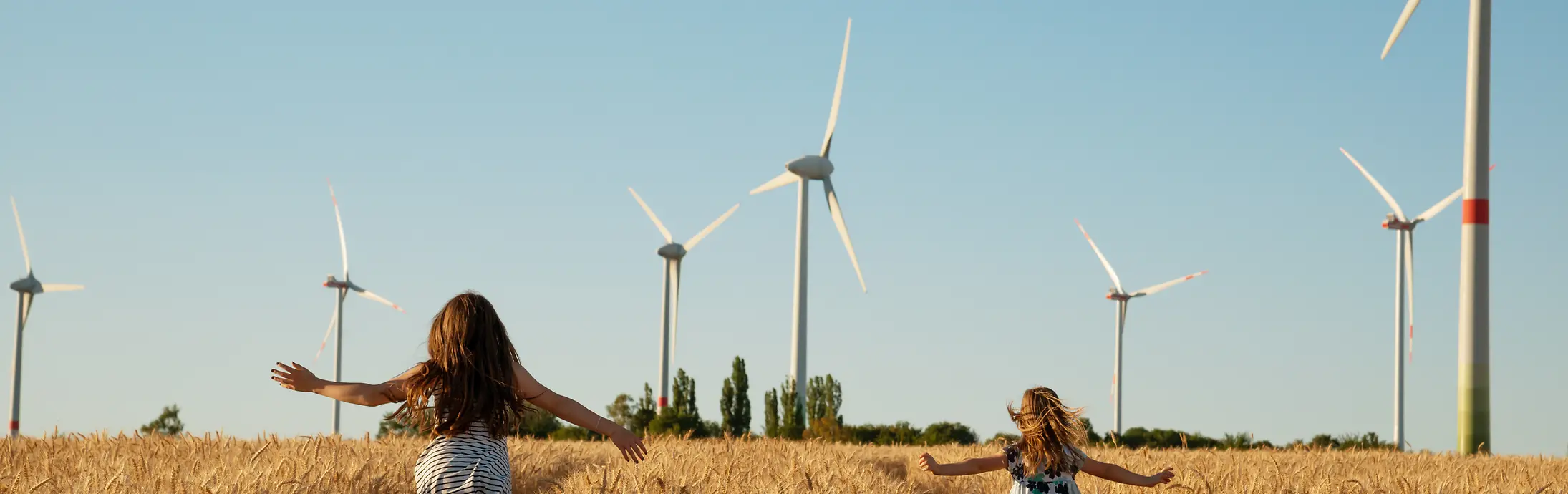 Dve dekleti, ki tečeta po koruznem polju s sodobnimi mlini na veter v ozadju