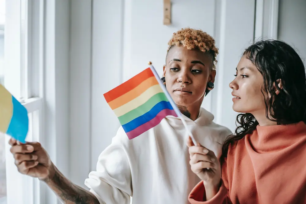 Dve ženski se pogovarjata, medtem ko držita zastavo LGBTQ+