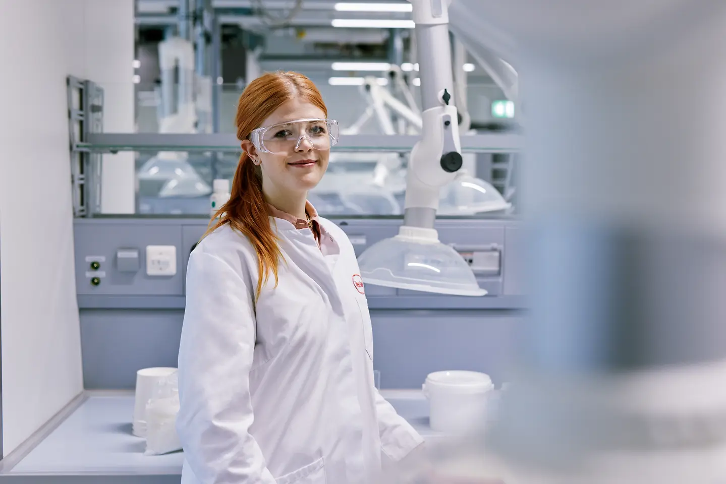 Diplomant, ki začenja kariero pri Henklu, oblečen v belo laboratorijsko haljo, stoji v sodobnem laboratorijskem okolju s tehnično opremo v ozadju.
